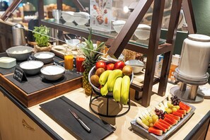 Un bufé de desayuno con diversas frutas, una máquina de café y un dispensador de jugo.