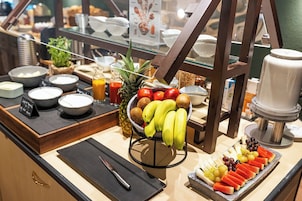 Buffet de café da manhã com diversas frutas, uma máquina de café e um dispensador de suco.