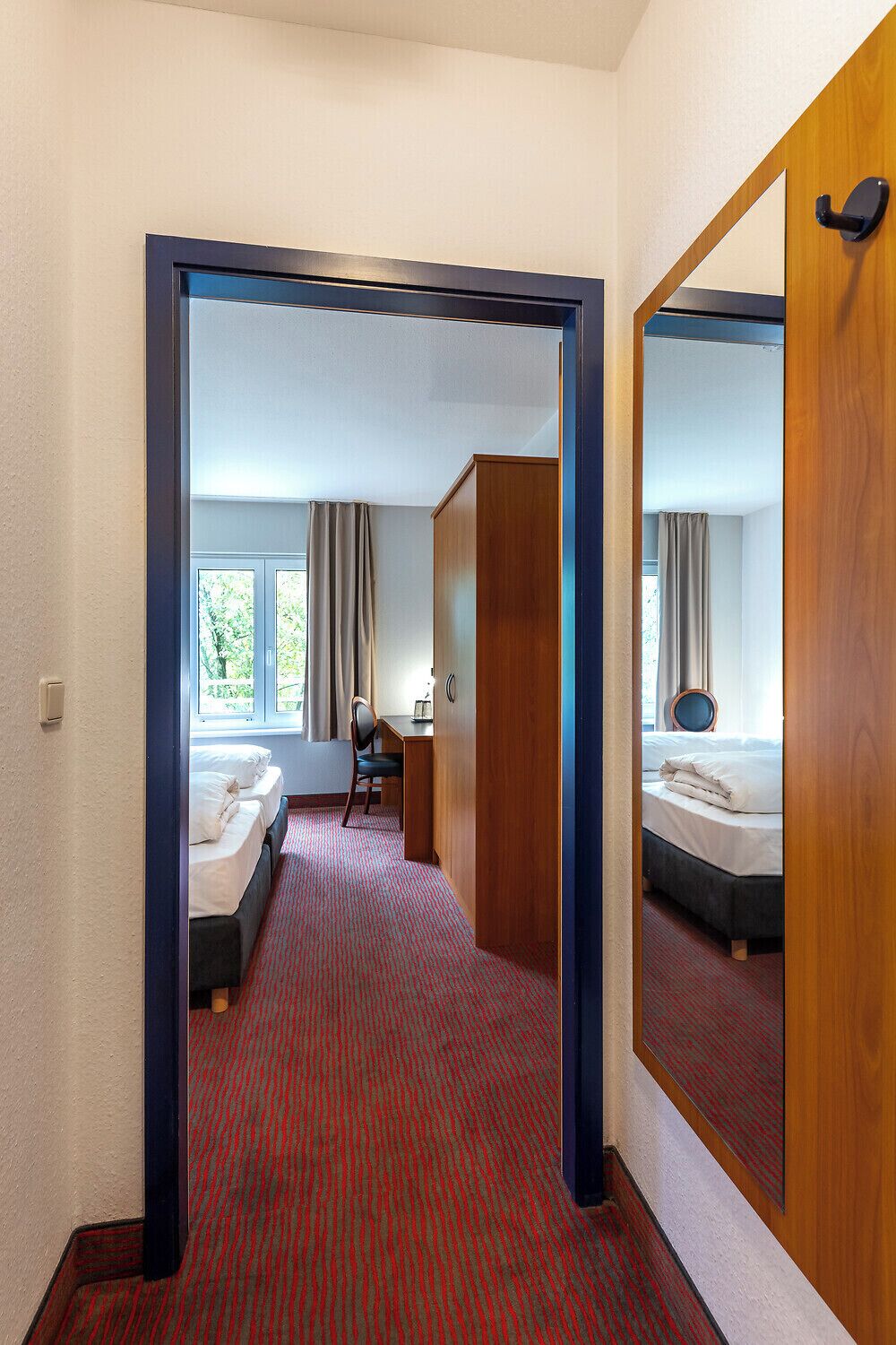 Habitación de hotel con alfombra roja, cama, escritorio y espejo.
