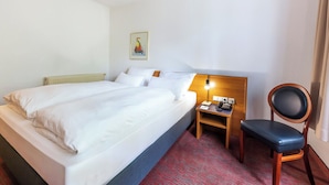 A hotel room with a bed, bedside table, lamp, chair, and a painting on the wall. - ACHAT Hotel Darmstadt Griesheim (Griesheim)