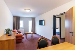 A hotel room with a wooden desk, a red sofa, a small table, and a TV mounted on the wall. - ACHAT Hotel Darmstadt Griesheim (Griesheim)