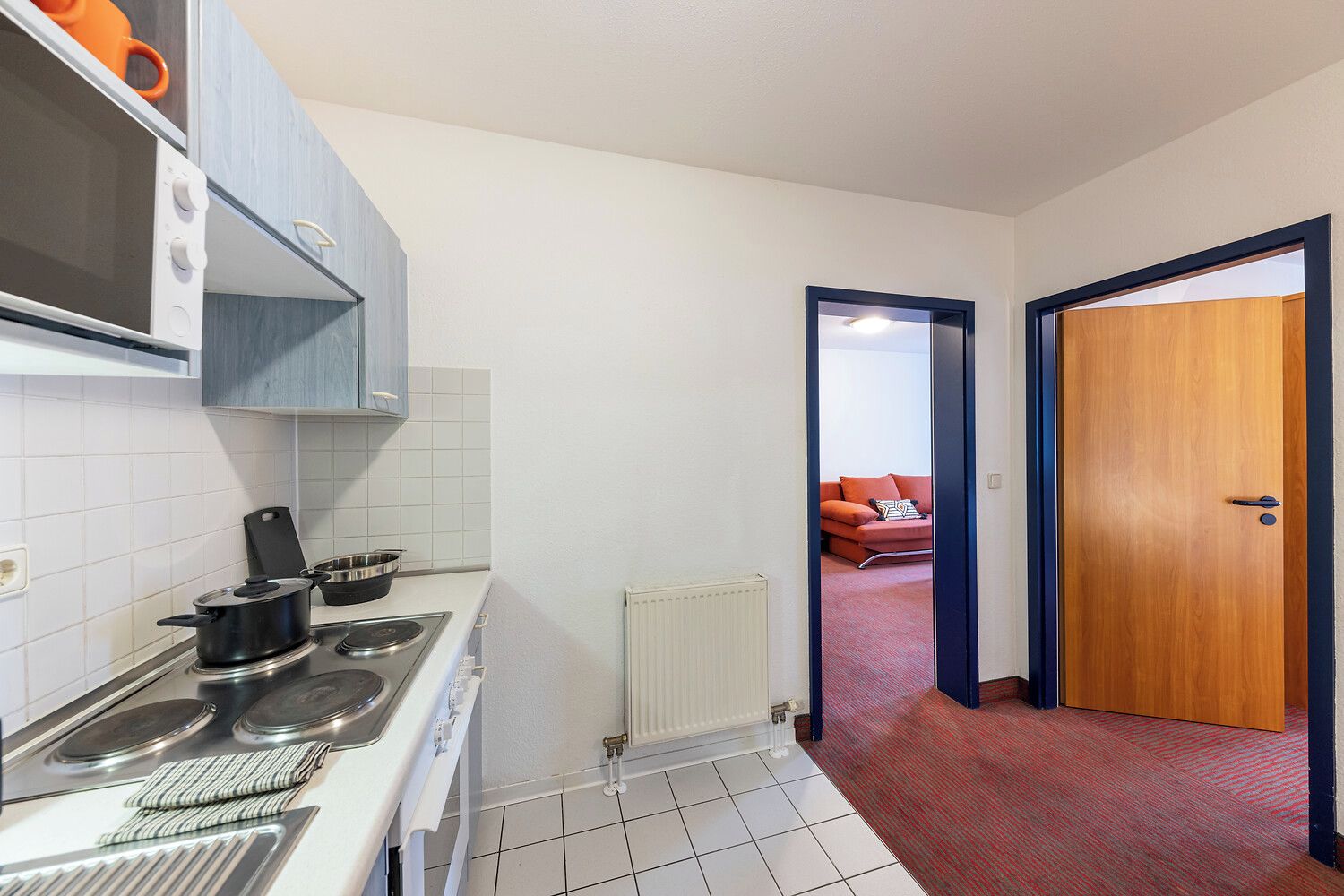 Cocina compacta con estufa, horno y microondas. Se ve un sofá rojo a través de un arco abierto en la zona de estar contigua.