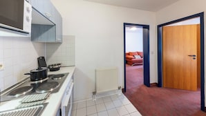 A compact kitchen with a stove, oven, and microwave. A red sofa is visible through an open doorway in the adjacent living area. - ACHAT Hotel Darmstadt Griesheim (Griesheim)