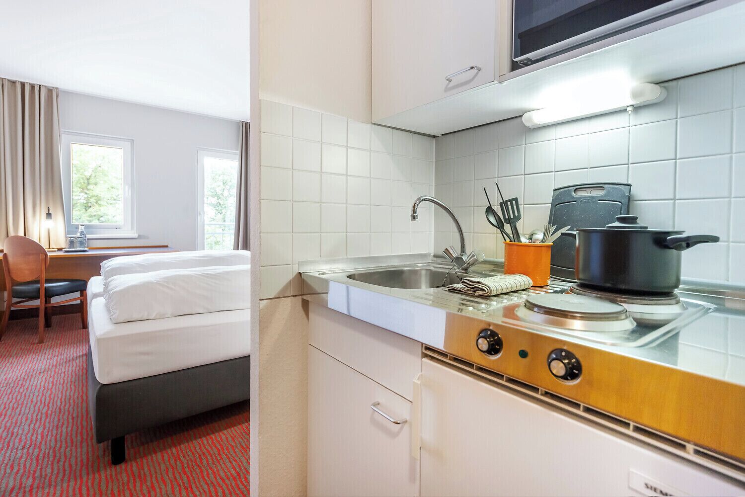 Een compacte hotelkamer met een kitchenette, een bed, een bureau en een raam.