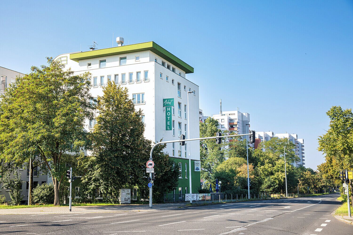 Un hotel con fachada verde y blanca, varios pisos y un cielo despejado.