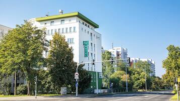 Un hotel con fachada verde y blanca, varios pisos y un cielo despejado.