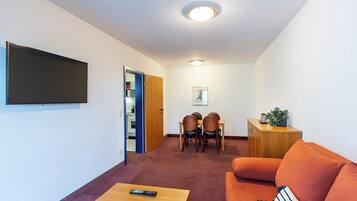 Un ambiente compatto con una TV a schermo piatto montata a parete, un'area pranzo con sedie e tavolo, e un divano con un cuscino.