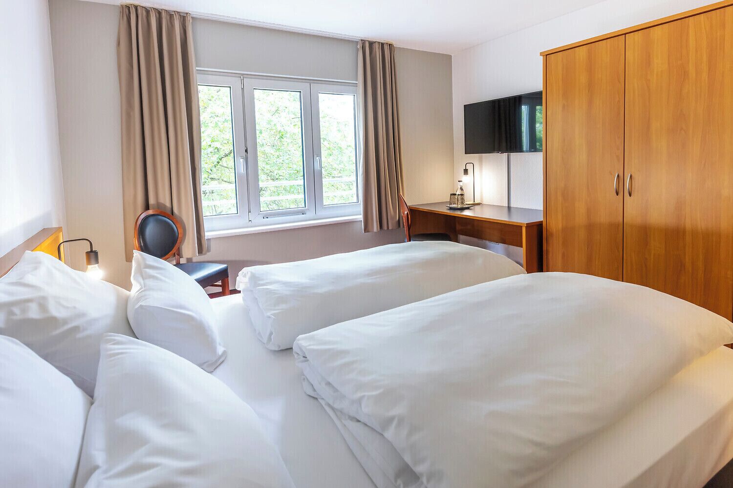 Habitación de hotel con dos camas, un escritorio, una silla, un televisor y un armario.