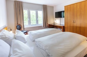 Quarto de hotel com duas camas, uma escrivaninha, uma cadeira, uma televisão e um guarda-roupa.