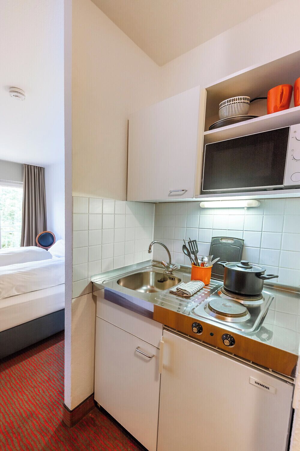 A compact hotel kitchen with a sink, stove, and a Siemens refrigerator.