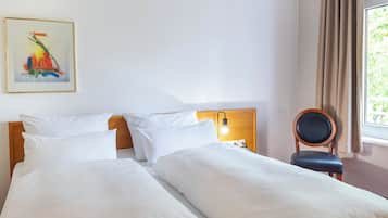 Ein Hotelzimmer mit zwei Betten, einem Nachttisch mit Lampe, einem Sessel und einem Bild an der Wand.