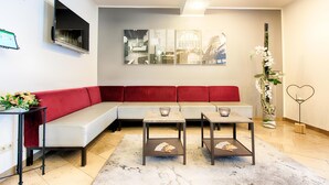 A modern living room with a red sofa, two small tables with magazines, a TV mounted on the wall, and a large abstract painting. - ACHAT Hotel Frankenthal in der Pfalz (Frankenthal)