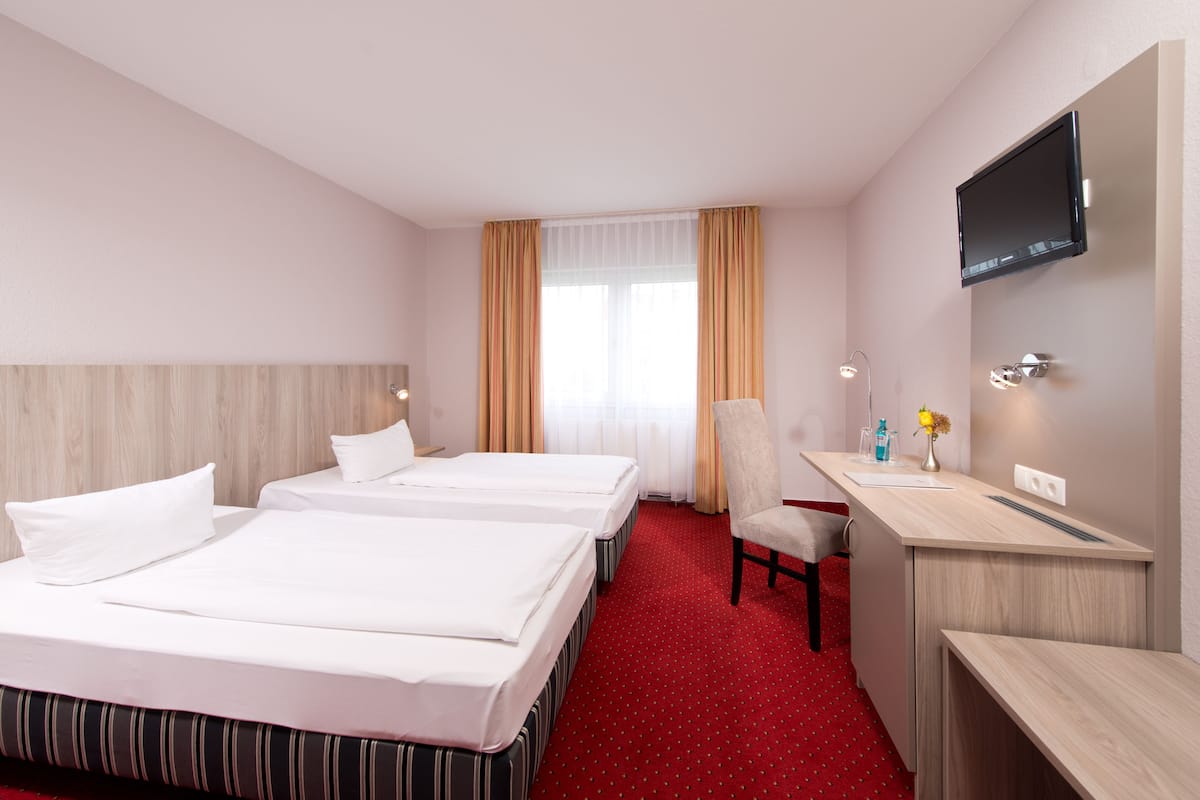 Habitación de hotel con dos camas, un escritorio, una silla, un televisor y una ventana con cortinas.