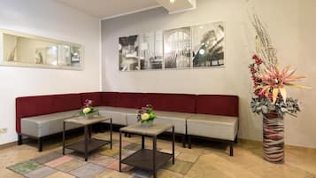 A modern waiting area with a grey sofa, two small tables with floral centerpieces, and a large decorative vase.