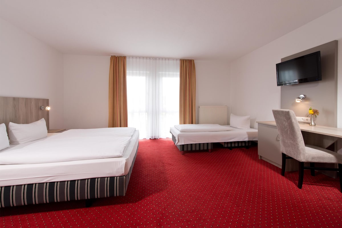 Una habitación de hotel con dos camas, un escritorio, una silla, un televisor y una ventana con cortinas.