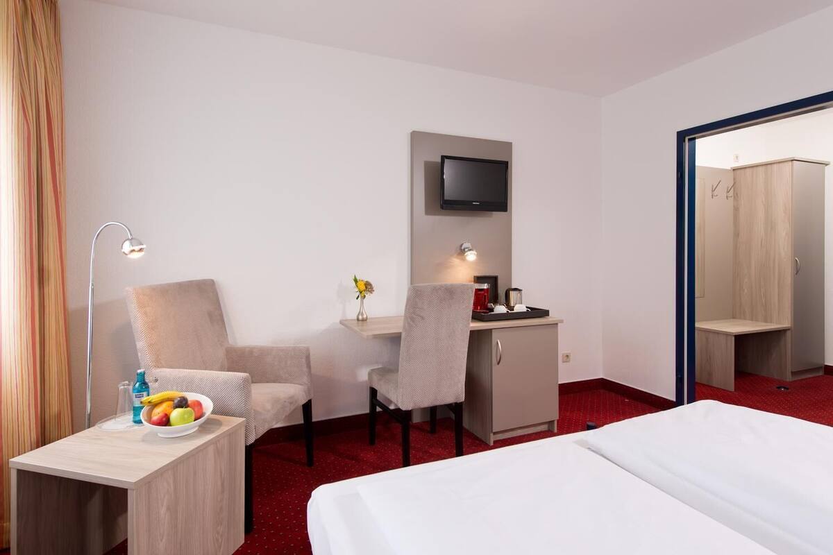 Habitación de hotel con cama, escritorio con silla, televisor montado en la pared y una mesita con frutero.