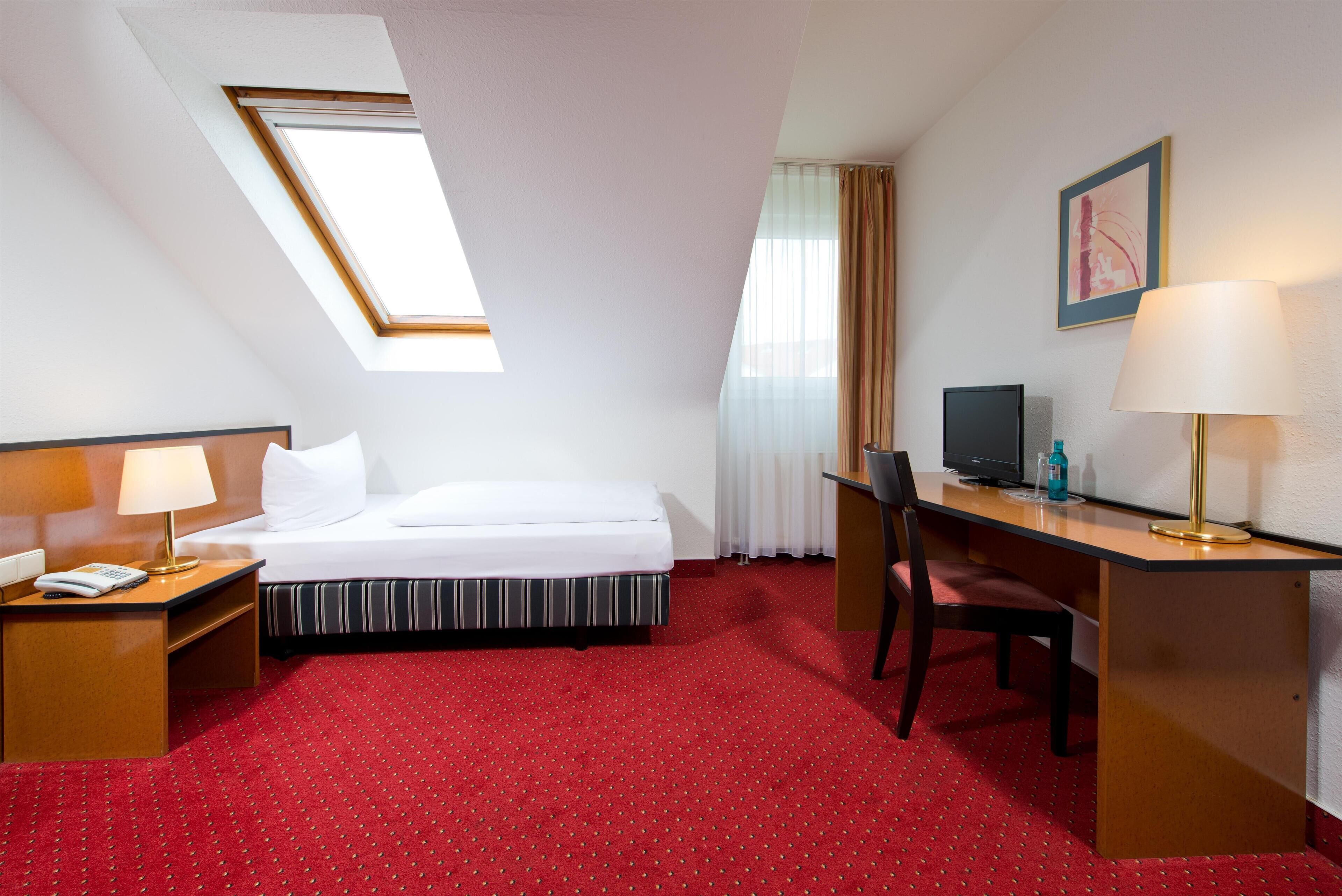 Een hotelkamer met een bed, bureau, stoel en dakraam.