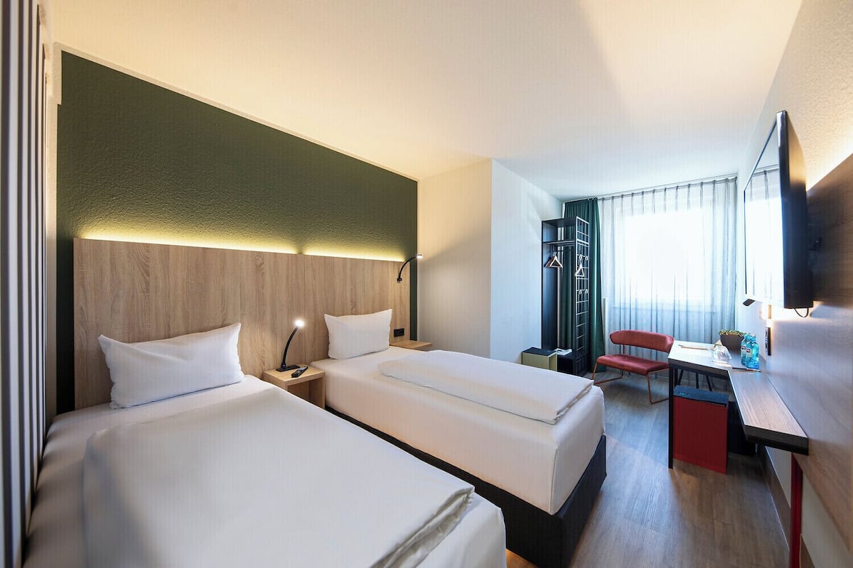 A hotel room with two beds, a desk, a chair, a TV, and a wardrobe.