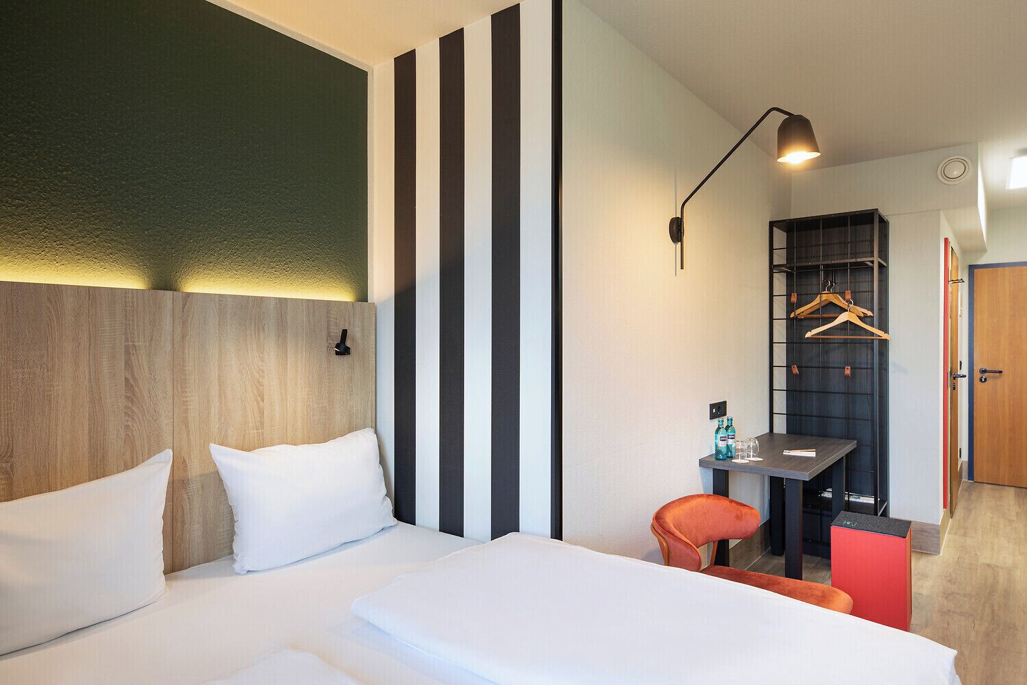 Una habitación de hotel moderna con una cama grande, un escritorio con silla, perchero y armario.
