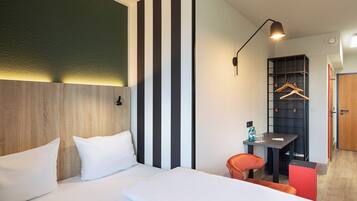 Una habitación de hotel moderna con una cama grande, un escritorio con silla, perchero y armario.