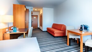 Una habitación de hotel con cama, escritorio con lámpara, sofá y mesa con tetera y vasos.