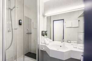 Un bagno moderno con cabina doccia in vetro, un lavandino bianco e uno specchio sopra.