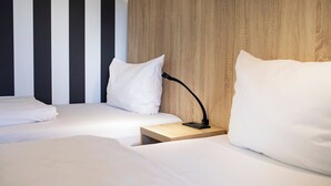 Habitación de hotel con dos camas, cabecera de madera, mesita de noche con lámpara y pared a rayas.