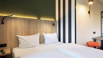 A hotel room with a wooden headboard, a bed with white linens, a nightstand with a remote control, a striped wall, and a small orange chair.