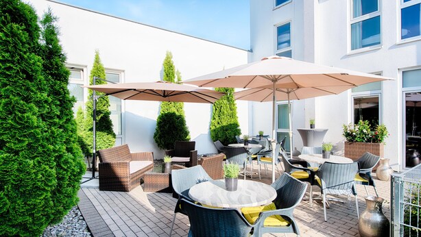 Un patio al aire libre con mobiliario de mimbre, sombrillas y plantas en macetas.