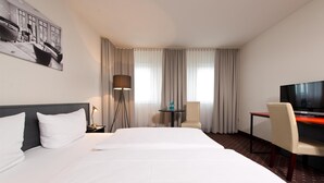 Una habitación de hotel con una cama grande, un escritorio, una silla, un televisor y una lámpara.