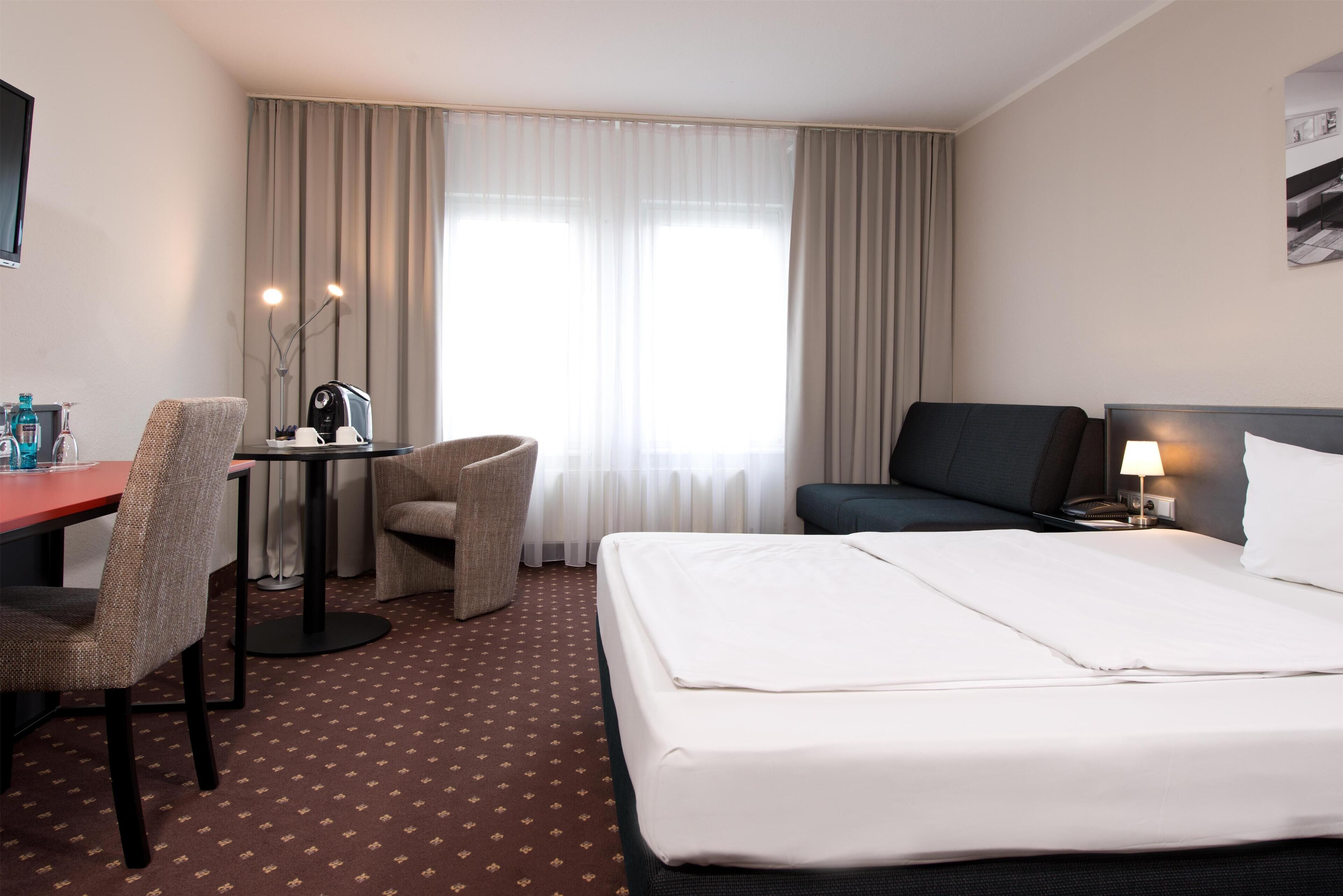 Habitación de hotel con cama, escritorio, sillón y televisor.