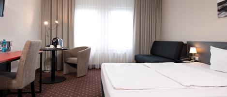 Habitación de hotel con cama, escritorio, sillón y televisor.