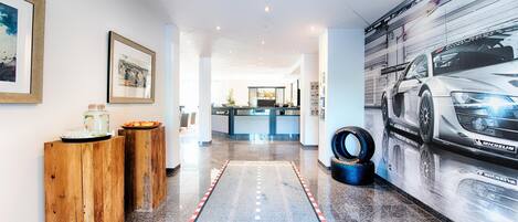 A hotel lobby with a polished granite floor, a reception desk, framed artwork on the walls, and a large automotive advertisement.