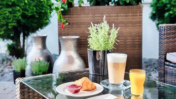 A table with a croissant, a glass of juice, and a drink, surrounded by potted plants and vases.