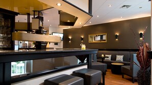 Un área de bar moderna con mostrador, taburetes y una zona de estar con sofá y mesas redondas.