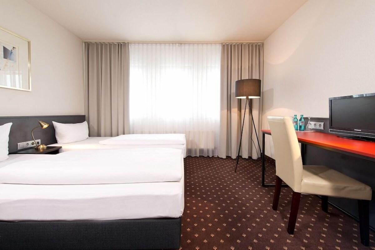 A hotel room with a bed, a desk, a chair, a television, and a floor lamp.