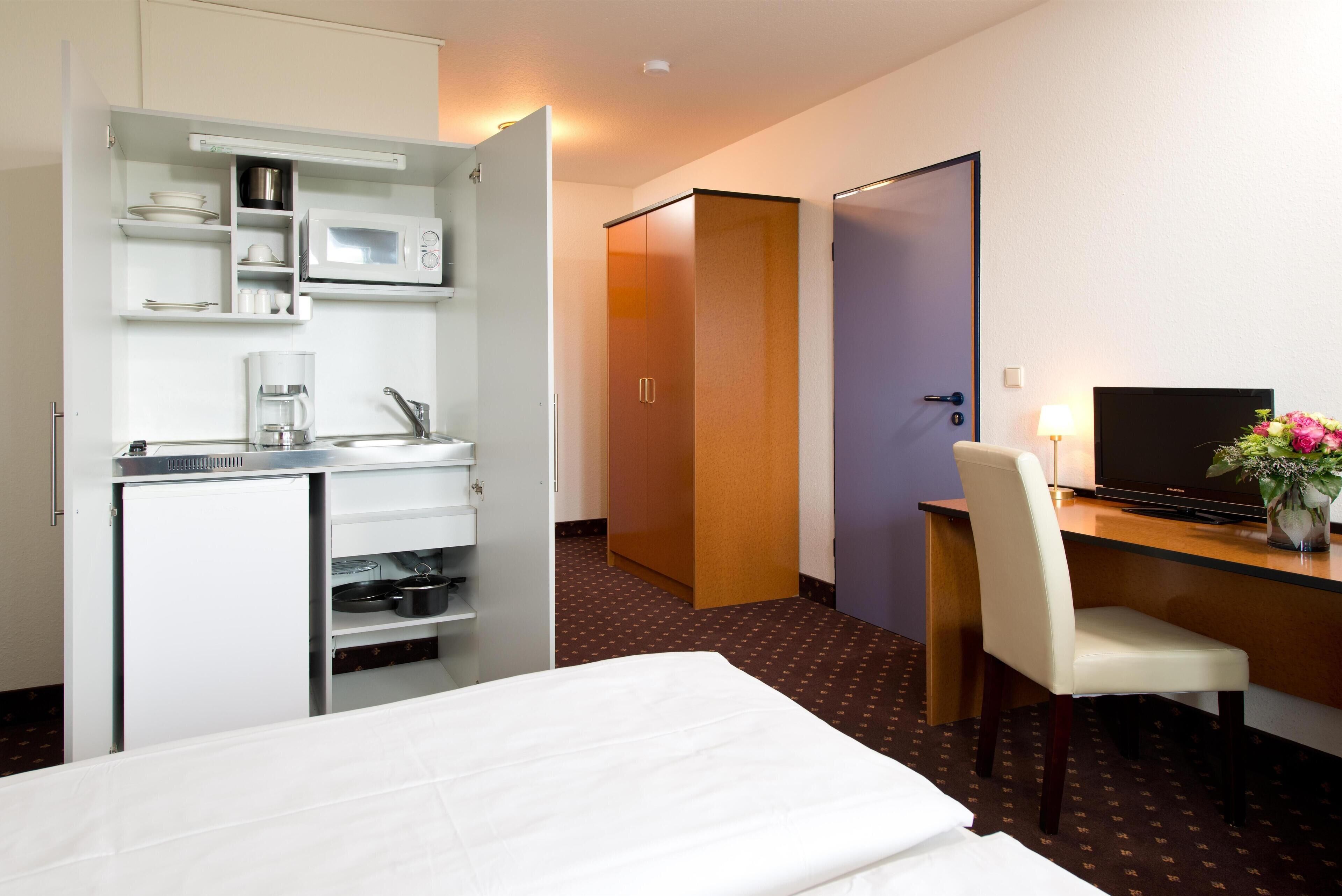 Habitación de hotel con cama, escritorio, silla, televisión, microondas y minibar.
