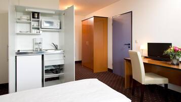 Habitación de hotel con cama, escritorio, silla, televisión, microondas y minibar.