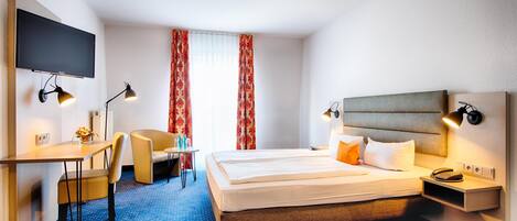 Una habitación de hotel con cama, escritorio, silla, televisor y ventana con cortinas.