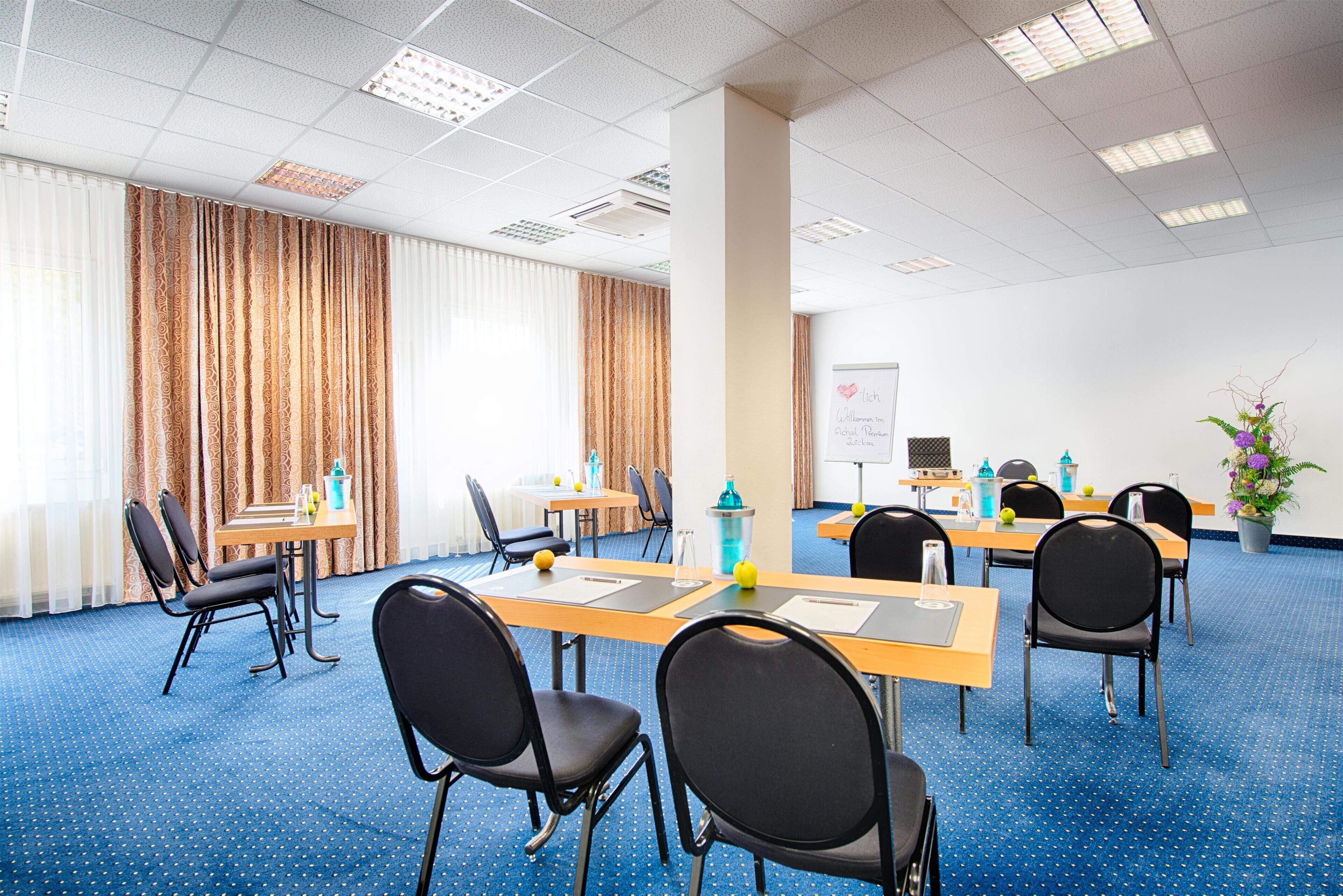 A conference room with a blue carpet, black chairs, wooden tables, and a whiteboard.
