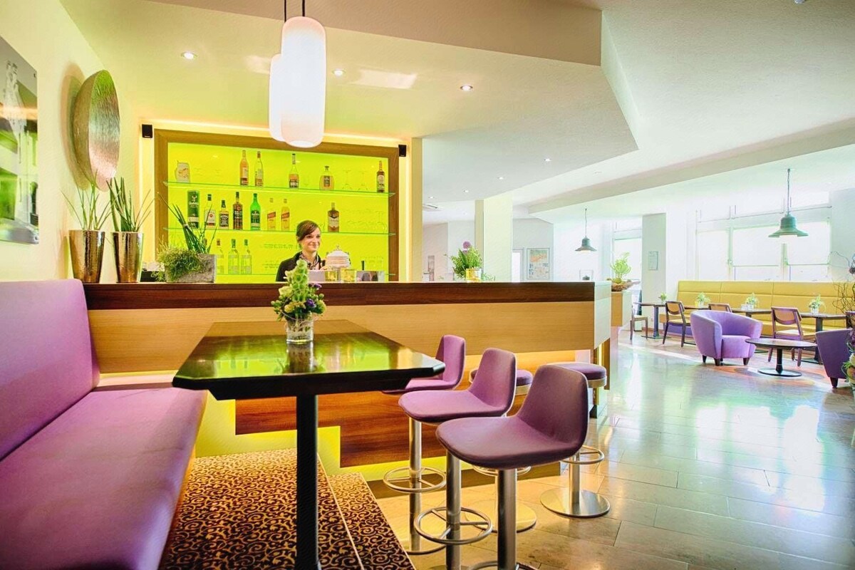 A hotel lobby with a reception desk, purple seating, and a bar area.