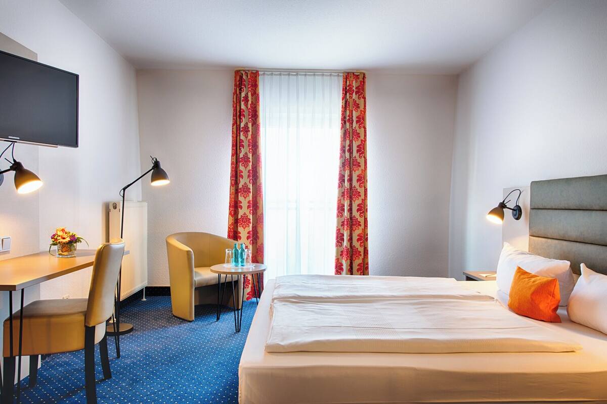 Une chambre d’hôtel avec un lit, un bureau, une chaise, une petite table avec des bouteilles et un téléviseur.