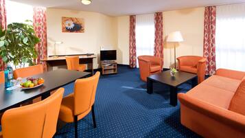 Een hotelkamer met een eethoek, twee oranje banken, een televisie en een potplant.