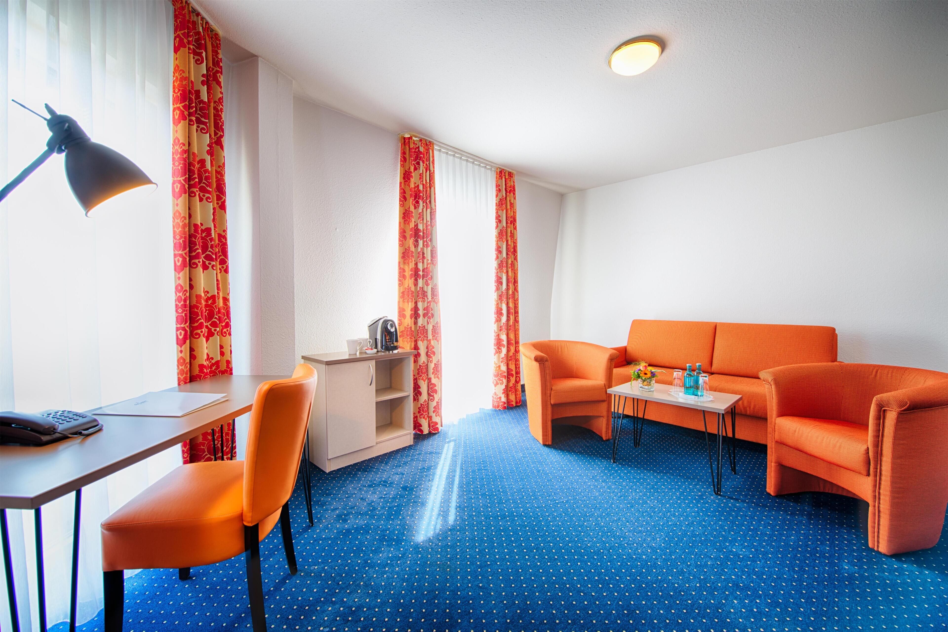 A room with a blue polka dot carpet, orange furniture, a desk with a lamp, and a small table with a vase and bottles.
