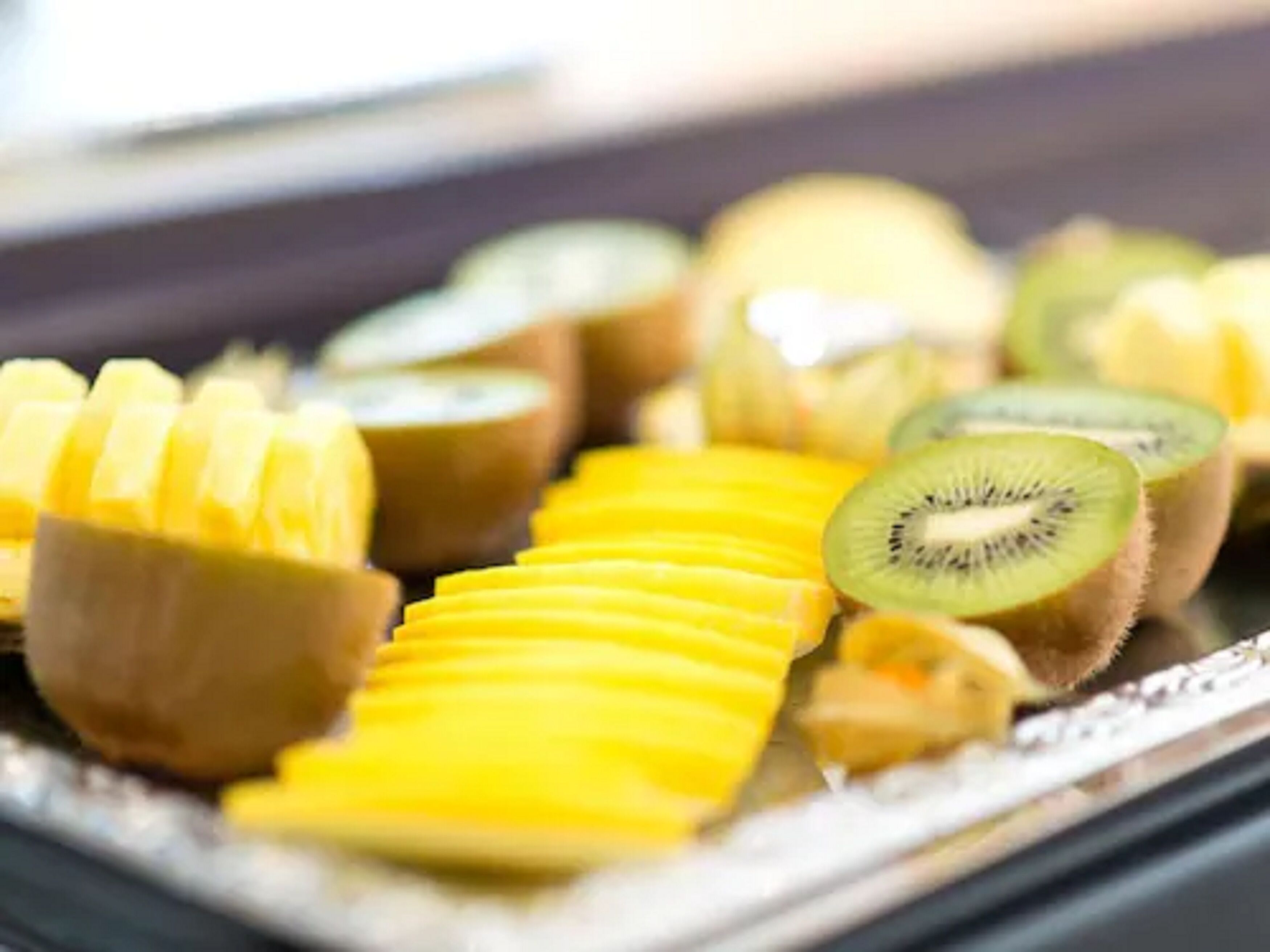 Una bandeja con frutas cortadas, como kiwi, mango y piña.