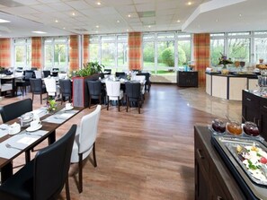 A spacious dining area with multiple tables and chairs, large windows with curtains, and a buffet counter with various food items. - ACHAT Hotel Zwickau (Zwickau)