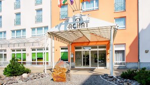 A hotel entrance with a covered entrance, multiple flags, and a stone sculpture. - ACHAT Hotel Zwickau (Zwickau)