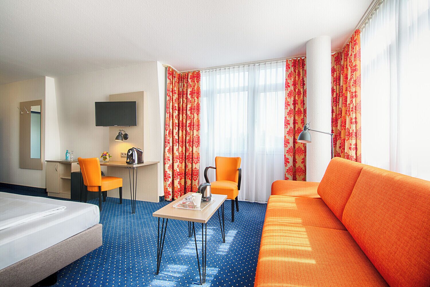 A hotel room with a bed, a desk with a chair, a sofa, and a TV.