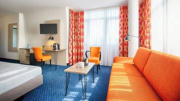 A hotel room with a bed, a desk with a chair, a sofa, and a TV.