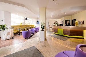 Un vestíbulo de hotel con una recepción, asientos morados y un diseño moderno.